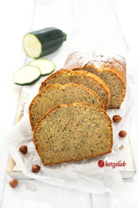 Saftiger Nuss-Zucchinikuchen auf einem Holzbrett. 3 Scheiben davon vor dem angeschnittenen Kuchen.
