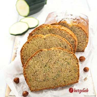 Saftiger Nuss-Zucchinikuchen auf einem Holzbrett. 3 Scheiben davon vor dem angeschnittenen Kuchen.