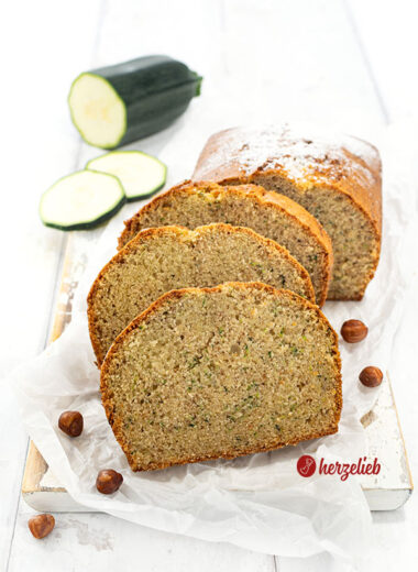Saftiger Nuss-Zucchinikuchen auf einem Holzbrett. 3 Scheiben davon vor dem angeschnittenen Kuchen.
