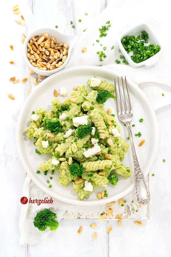 Grüne Brokkoli-Pasta auf einem Teller mit hohem Rand. Dekoriert mit Pinienkernen, Brokkoli und Feta. 