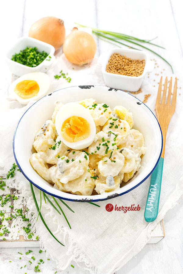 Cremiger und schneller Schmand-Kartoffelsalat in einer Emailleschüssel. Dekoriert mit Senfsaat, Schnittlauchröllchen und Ei