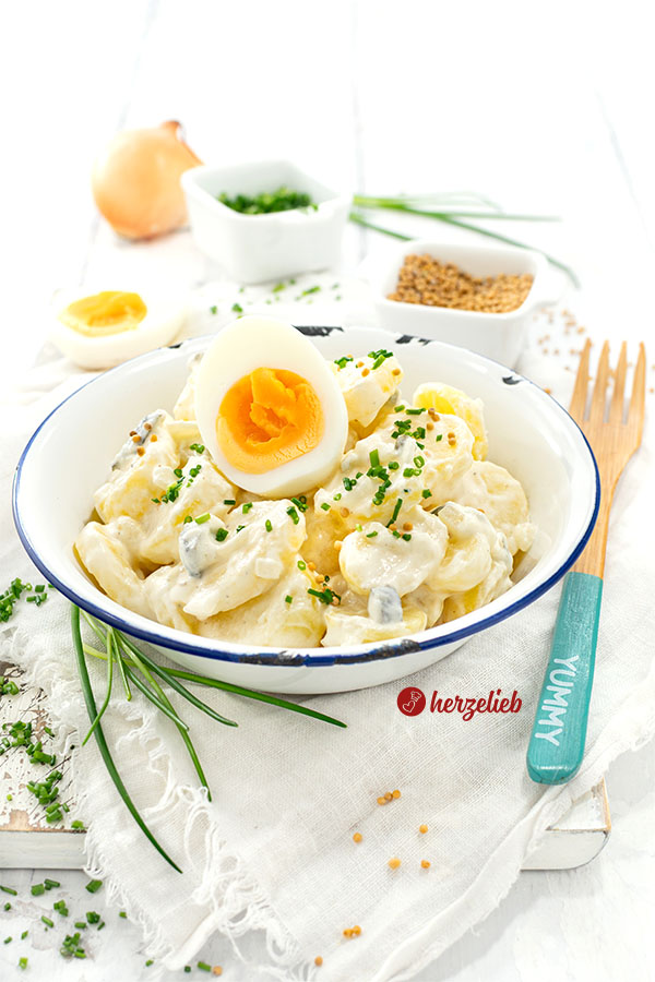 Cremiger Schmand-Kartoffelsalat in einer Schüssel. Dekoriert mit Ei und Schnittlauchröllchen