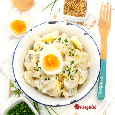 Eine Schale Schmand-Kartoffelsalat. Dekoriert mit Schnittlauchröllchen und Ei.