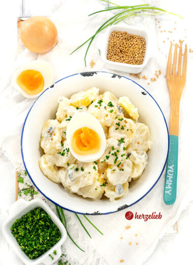 Eine Schale Schmand-Kartoffelsalat. Dekoriert mit Schnittlauchröllchen und Ei.