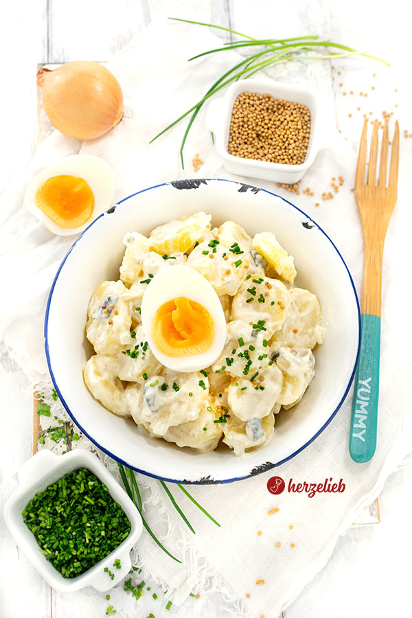 Eine Schale Schmand-Kartoffelsalat. Dekoriert mit Schnittlauchröllchen und Ei. 