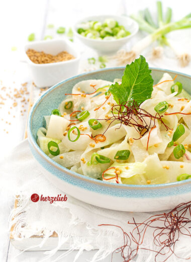 Eine Schüssel Kohlrabi-Salat nach einem Schüttel-Kohlrabi Rezept von herzelieb. Dekoriert mit einem Kohlrabiblatt, Senfsaat, Frühlingszwiebeln und Chilifäden.