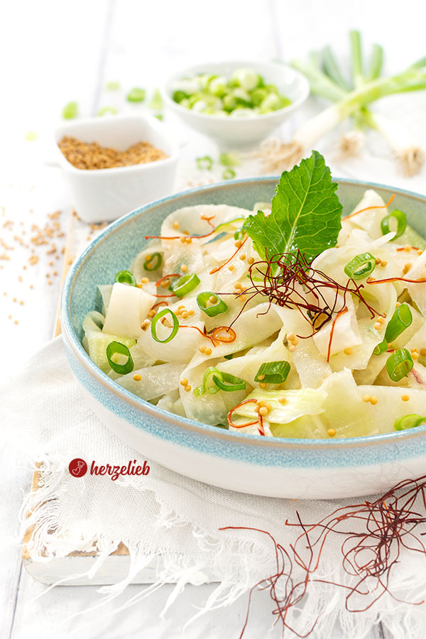 Eine Schüssel Kohlrabi-Salat nach einem Schüttel-Kohlrabi Rezept von herzelieb. Dekoriert mit einem Kohlrabiblatt, Senfsaat, Frühlingszwiebeln und Chilifäden.