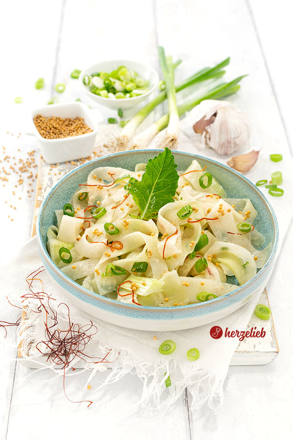 Kohlrabi-Salat Rezept für Schüttel-Kohlrabi. Dekoriert mit Senfkörner, Chilifäden und einem Kohlrabiblatt. Angerichtet in einer Schale.