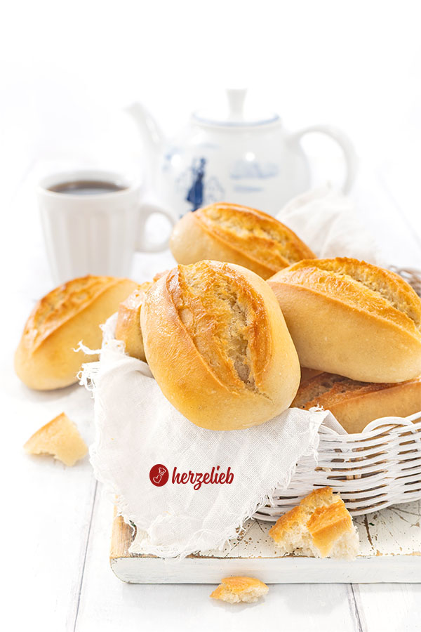 Ein Körbchen mit Brötchen nach einem Sonntagsbrötchen Rezept von herzelieb. Im Hintergrund Kaffeebecher und eine Kanne. 