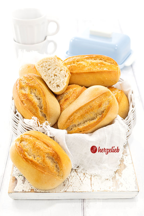 Brötchen nach einem Sonntagsbrötchen Rezept von herzelieb in einem Korb. Im Hintergrund eine Butterglocke und Tasssen