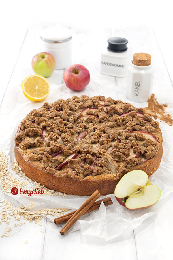 Ein ganzer Apfelkuchen mit streuseln nach einem Apfel-Kladdkaka Rezept von herzelieb. Angerichtet mit Zimtstangen, Äpfeln, Zitronen und Gewürzgefäßen