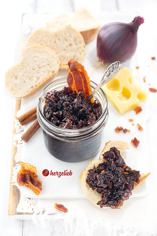 Ein Gläschen Speckmarmelade nach einem Bacon Jam Rezept von herzelieb. Angerichtet mit Brot und Käse. Dekoriert mit einer Zwiebeln, knusprigen Speck und Zimtstangen