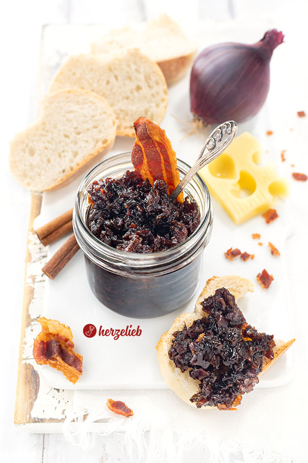 Ein Gläschen Speckmarmelade nach einem Bacon Jam Rezept von herzelieb. Angerichtet mit Brot und Käse. Dekoriert mit einer Zwiebeln, knusprigen Speck und Zimtstangen