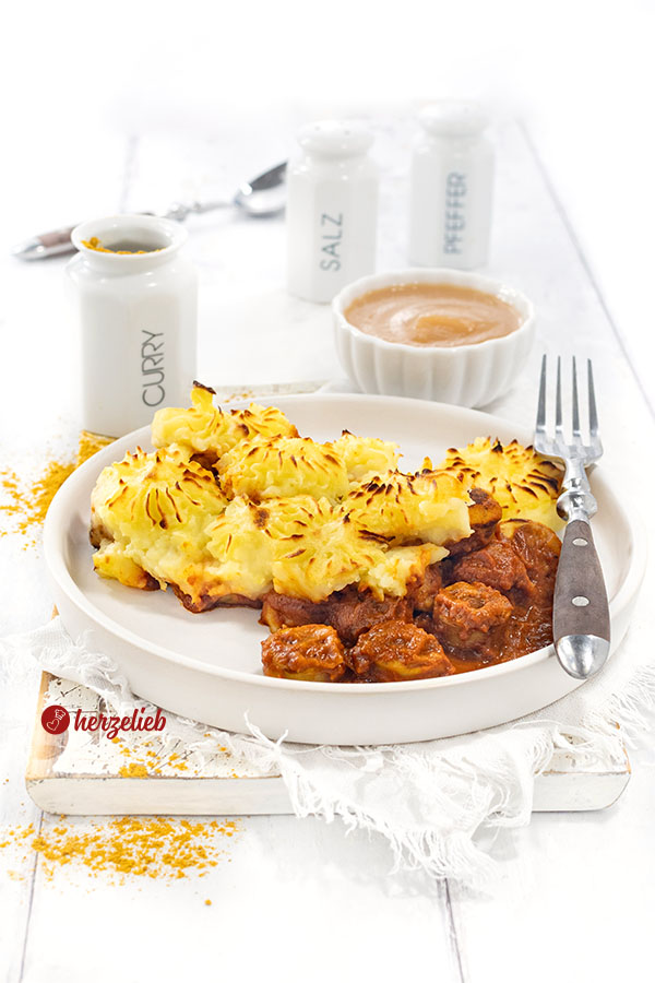 Ein Teller mit Currywurstauflauf mit Bratwurst in Currysoße und einer Kartoffelhaube