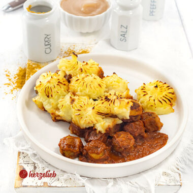 Teller mit einem Auflauf nach einem Currywurstauflauf Rezept. Der Auflauf hat eine Kartoffelhaube