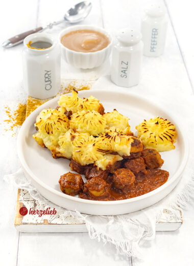 Teller mit einem Auflauf nach einem Currywurstauflauf Rezept. Der Auflauf hat eine Kartoffelhaube