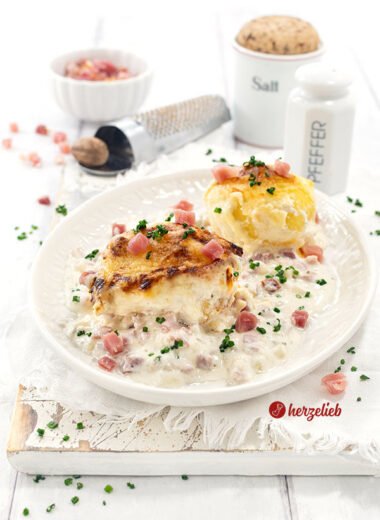 Ein Teller mit 2 mit Käse überbackenen Kartoffeln nach einem Flammkuchen-Kartoffeln Rezept von herzelieb. Angerichtet mit viel heller Soße.