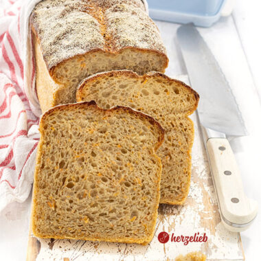 Saftiges Kartoffel-Karotten-Brot. Im Hintergrund steht auf auf der Schnittfläche der angeschnittene Brotlaib. Davor 2 Scheiben von dem Brot.