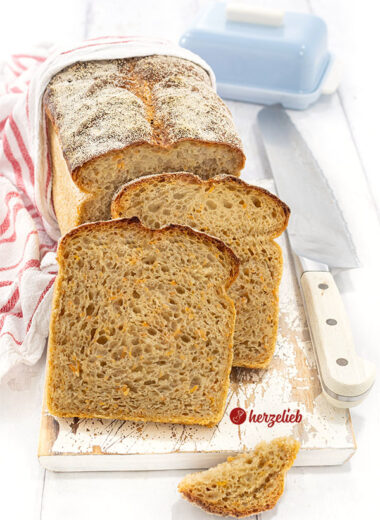Saftiges Kartoffel-Karotten-Brot. Im Hintergrund steht auf auf der Schnittfläche der angeschnittene Brotlaib. Davor 2 Scheiben von dem Brot.