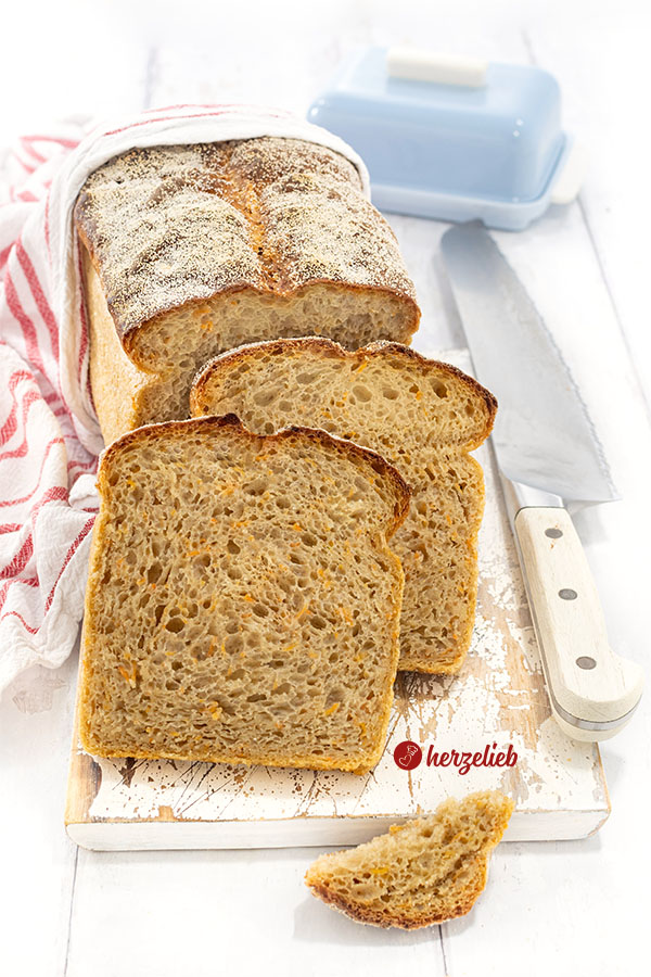 Saftiges Kartoffel-Karotten-Brot. Im Hintergrund steht auf auf der Schnittfläche der angeschnittene Brotlaib. Davor 2 Scheiben von dem Brot.