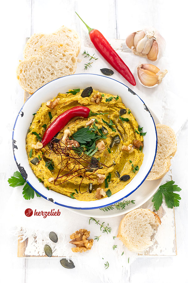 Eine Schale mit einem Dip nach einem Ofenkürbis-Dip mit Feta Rezept von herzelieb. Angerichtet mit Chilifäden, roter Chilischote, Petersilie, Walnüssen und Kürbiskernen. Serviert mit Brot.
