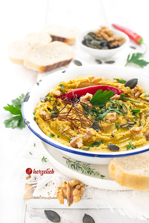 Eine Schüssel mit einem Dip nach einem Ofenkürbis-Dip mit Feta Rezept von herzelieb. Dekoriert mit Petersilie, roter Chili, Walnüssen, Kürbiskernen und Chilifäden.