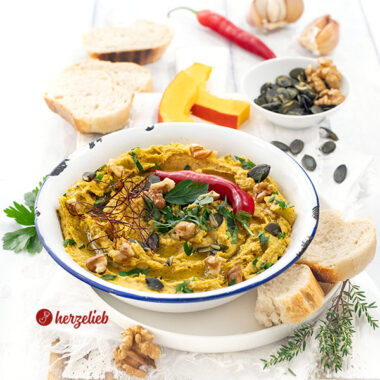 Eine Emailleschüssel mtit Ofenkürbis-Dip mit Feta. Serviert mit Brot, dekoriert mit Walnüssen, Kürbiskernen, Chilifäden, Petersilie und roter Chilischote.