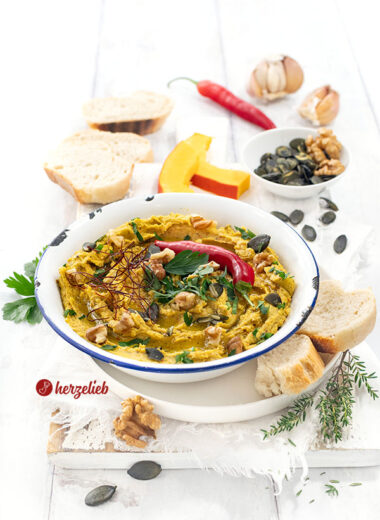 Eine Emailleschüssel mtit Ofenkürbis-Dip mit Feta. Serviert mit Brot, dekoriert mit Walnüssen, Kürbiskernen, Chilifäden, Petersilie und roter Chilischote.