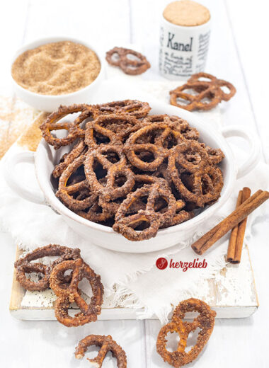 Eine Schüssel mit Knabberkram nach einem Rezept für gebrannte Salzbrezeln von herzelieb. Dekoriert mit Zimtstangen. Im Hintergrund Gewürzgefäße