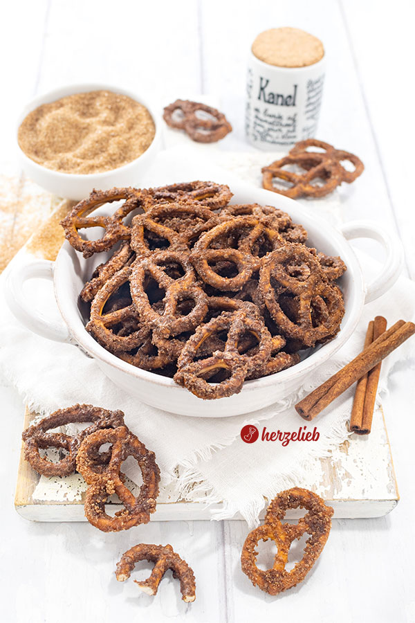 Eine Schüssel mit Knabberkram nach einem Rezept für gebrannte Salzbrezeln von herzelieb. Dekoriert mit Zimtstangen. Im Hintergrund Gewürzgefäße