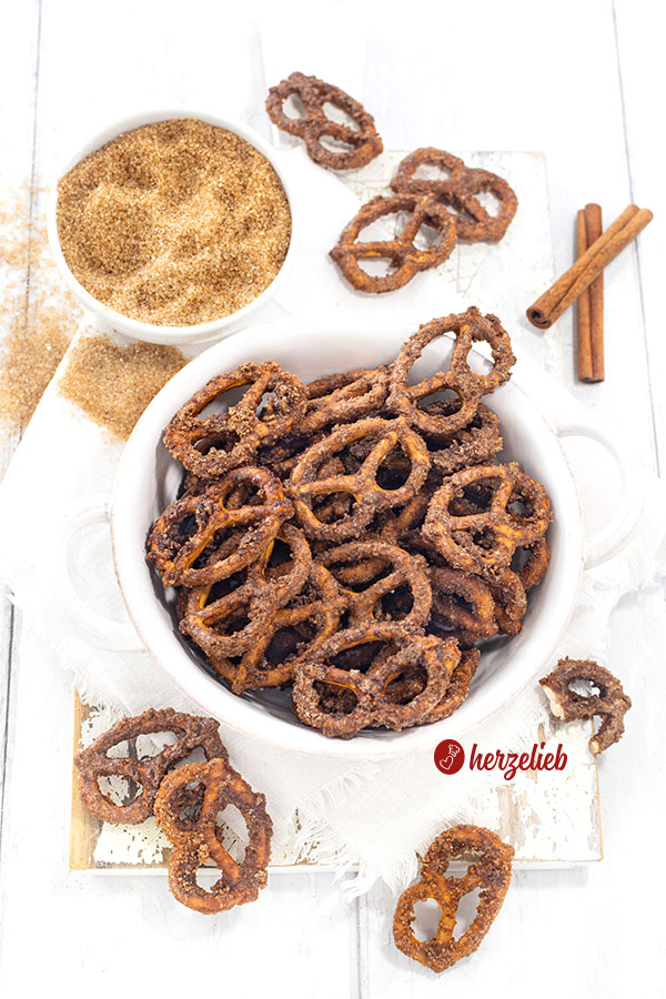 Eine Schale mit einem Knabbersnack nach einem Rezept für gebrannte Salzbrezeln von herzelieb. Dekoriert mit braunem Zucker und Zimtstangen.