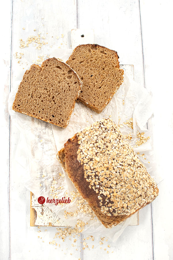 2 Scheiben von einem Dinkelbrot mit Haferflocken nach einem Hafer-Dinkel-Kastenbrot Rezept von herzelieb. Davor ein Brotlaib.
