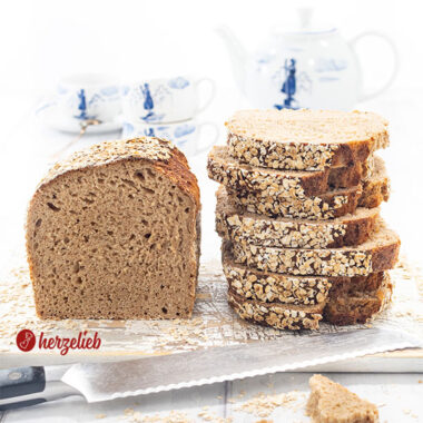 Ein Dinkelbrot, das mit Haferflocken nach einem Hafer-Dinkel-Kastenbrot Rezept von herzelieb. Links der Brotlaib und rechts ein Stapel mit Scheiben davon.