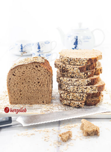 Ein Dinkelbrot, das mit Haferflocken nach einem Hafer-Dinkel-Kastenbrot Rezept von herzelieb. Links der Brotlaib und rechts ein Stapel mit Scheiben davon.
