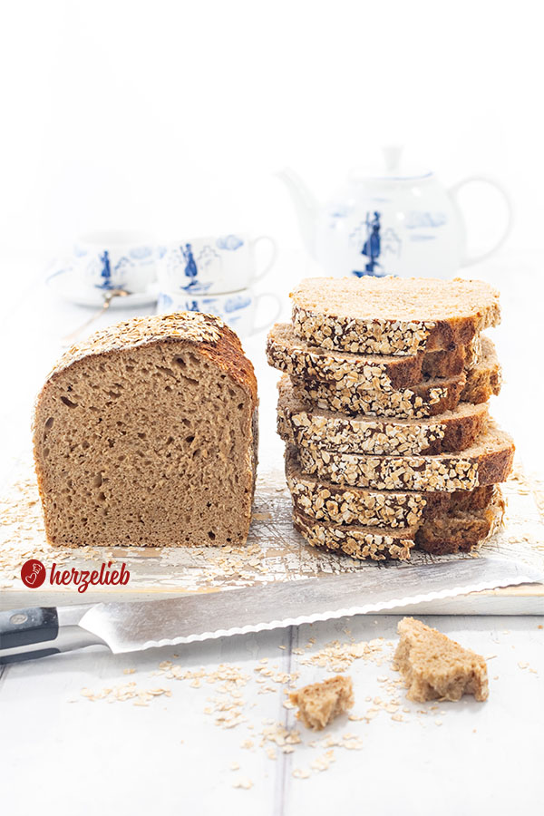 Ein Dinkelbrot, das mit Haferflocken nach einem Hafer-Dinkel-Kastenbrot Rezept von herzelieb. Links der Brotlaib und rechts ein Stapel mit Scheiben davon.
