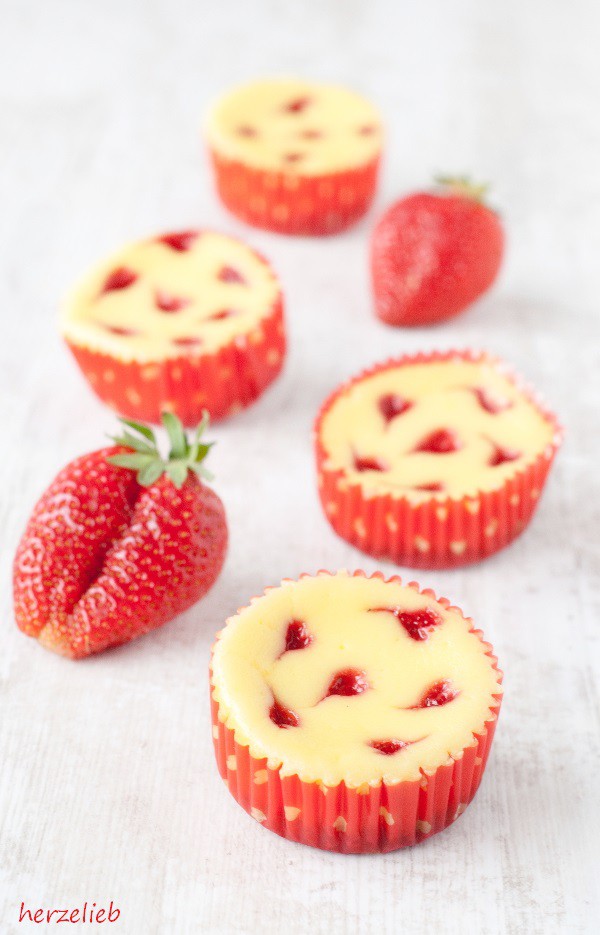 4 Käsekuchenmuffins in roten Muffinformen mit Erdbeerherzchen. Dekoriert mit 2 Erdbeeren. Käsekuchen-Muffins Rezept von herzelieb